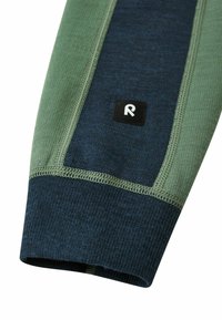 Anpassbare Sportärmel aus gemischten dunkelblauen und grünen Stoffen. Mit einer strukturierten Oberfläche, sichtbaren Nähten und einem schwarzen Logotag.