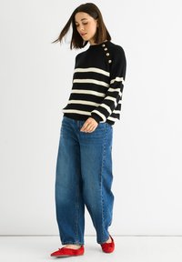 Black and white striped sweater with a ribbed texture, featuring gold buttons on the shoulder. Paired with wide-leg blue jeans and red flats.