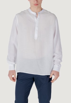 Camisa blanca ligera de manga larga con cuello tipo banda, tapeta de botones y textura ligeramente transparente, combinada con pantalones oscuros.