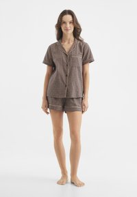 Conjunto de pijama a cuadros marrón y beige con una parte superior de botones de manga corta y pantalones cortos a juego, adornado con ribetes de color sólido.