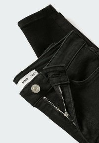 Černé džínové kalhoty s zipem, stříbrnými doplňky a tkanou etiketou uvnitř pasu. Tkanina se zdá být hladká a mírně pružná.