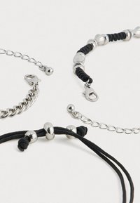 Tres pulseras con cuentas de metal plateado y cordón negro. Incluye una pulsera de cadena y un diseño trenzado con cierres seguros.