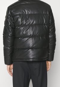 Svart puffjacka i glänsande material, med horisontella quiltade paneler och avslappnad passform. Har en minimalistisk design utan synlig hårdvara.