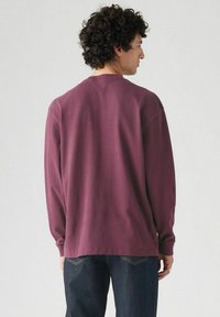 Camisa de manga larga de algodón burdeos. Corte relajado con puños de punto y cuello redondo, con una textura suave y un diseño sencillo.