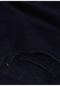 Donker denim stof met een subtiele textuur. Bevat een zakopening met contrasterende stiksels en een klein metalen klinknagel detail.
