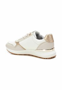 Zapatilla deportiva blanca y beige con un upper texturizado, acentos dorados y una suela de goma gruesa. Cuenta con cordones y un collar acolchado.