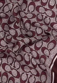 Foulard en soie présentant un motif répétitif de formes ovales marron et brun foncé sur un fond texturé blanc, avec une bordure brune.