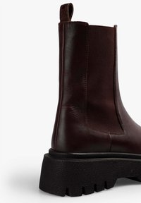 Bota Chelsea de cuero marrón oscuro con panel lateral elástico, tira de agarre y suela gruesa negra texturizada.