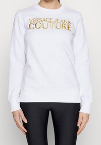 Felpa bianca in cotone, con ricamo dorato "VERSACE JEANS COUTURE" sul davanti, colletto a giro e polsini a coste.
