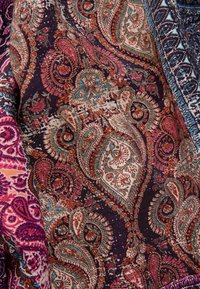 Tessuto con motivo paisley multicolore che presenta disegni intricati in tonalità di rosa, teal e arancione su uno sfondo scuro con texture.