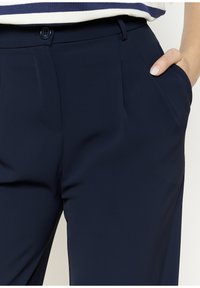 Navy trousers made of smooth fabric, featuring side pockets, a button closure, and subtle stitching detail. Tailored fit with a clean design.