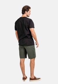 Camiseta de algodón negra, de manga corta, combinada con pantalones cortos verdes y zapatillas marrones con suelas blancas. Diseño simple y casual.