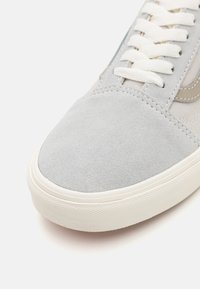 Baskets en suède gris avec un nez arrondi, semelle en caoutchouc blanche contrastante et lacets plats, présentant un léger accent sur le côté et des détails cousus.