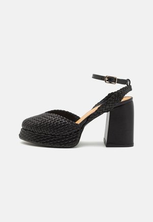 Sandale plateforme en cuir tressé noir avec talon bloc épais et sangle de cheville réglable avec boucle dorée.