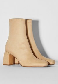 Stivali alla caviglia in suede beige con punta quadrata e tacco a blocco. Il design presenta una texture liscia e dettagli di cucitura minimali.