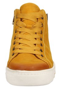 Zapatilla alta de cuero amarillo con punta redonda, superficie texturizada, acentos serrados, cordones planos y suela de goma blanca. Detalle de cremallera en el lateral.