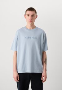 Light blue cotton t-shirt with short sleeves, round neck, and embossed "Calvin Klein" logo on the front; relaxed fit and smooth texture.