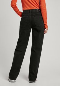 Höga svarta denimjeans med rak ben-design, två bakfickor och en lätt textur, matchat med en orange långärmad topp.