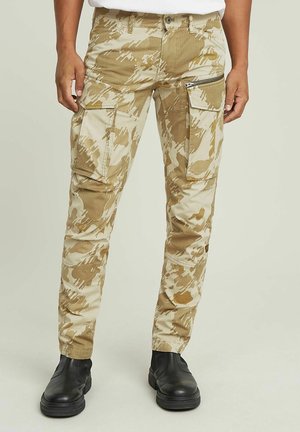 Beige camo cargo pants with multiple pockets, zip closure, and tapered legs. Made from textured fabric; paired with black boots.