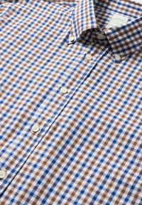Chemise à carreaux marron, bleue et blanche, boutonnée, avec un col classique, étalée à plat.