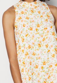 Blommig ärmlös klänning i lätt tyg, med orange och rosa blommor på en vit bakgrund, med hög halsringning och avslappnad passform.