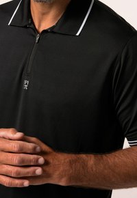 Polo noir avec un col zippé, agrémenté d'accents blancs sur le col et les manches. Tissu doux avec une coupe ajustée.