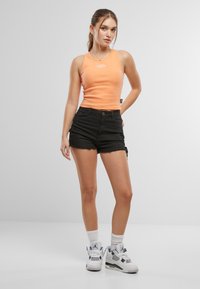 Oransje tanktopp, svarte denimshorts med detalj på siden, og hvite sneakers med grå detaljer. Settet har en tettsittende design og en uformell stil.