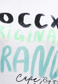 Weißes Stoff-T-Shirt mit schwarzem und türkisfarbenem Text in unterschiedlicher Stärke. Enthält die Wörter "Original" und "Cape Reg." in verspielter, fetter Schrift.