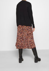 Svart stickad tröja med ribbad nederkant, ihop med en svävande midiklänning med ett blommönster i orange, vitt och svart. Svarta ankelstövlar.