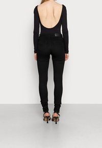 Svart långärmad bodysuit med låg ryggdesign, tillsammans med figurnära svarta jeans och svarta högklackade sandaler.