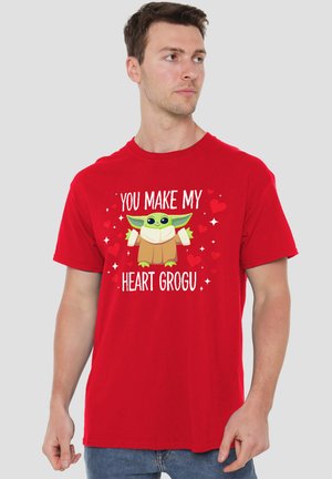 Man wearing red t-shirt with green cartoon character and text "You make my heart Grogu" surrounded by red hearts and sparkles.