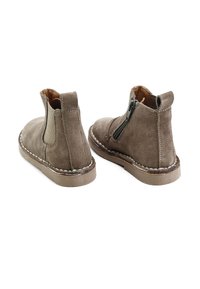 Botines de ante marrón con punta redondeada, paneles laterales elásticos y cierre de cremallera. Presentan costuras blancas contrastantes a lo largo de la suela.