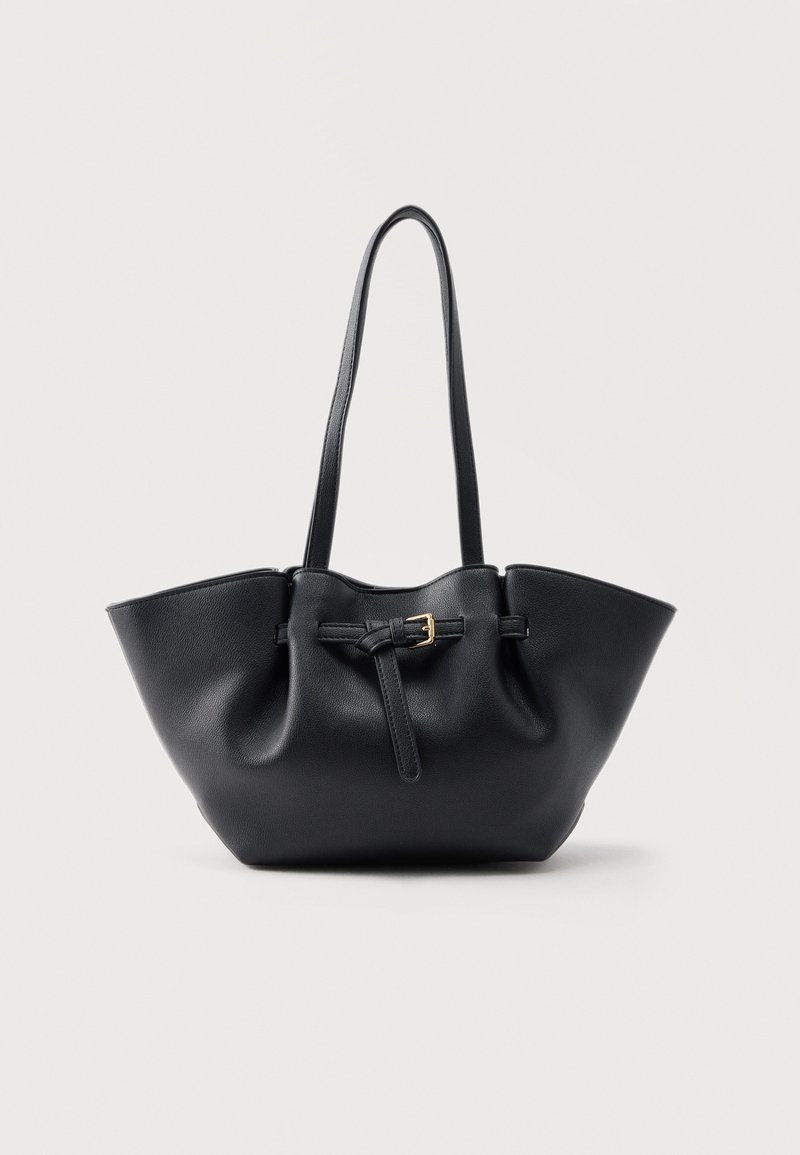 Sac cabas en cuir noir avec longues poignées et une lanière avant ornée d'une petite boucle dorée, sur fond uni.