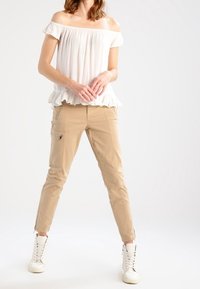 Bílý top bez ramínek s volánkovým lemem, béžové cargo kalhoty s kapsami a bílé vysoké tenisky se zipy.