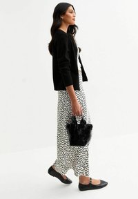 Zwarte cardigan over een witte top, gecombineerd met een witte rok met zwarte stippen. Geaccessoireerd met een kleine geweven zwarte handtas en zwarte ballerina's.
