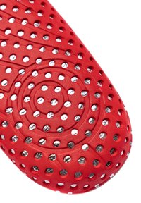 Red rubber product with circular perforations, featuring metallic accents inside the holes, textured surface, and a spiral design.