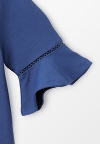 Blaue Kleidungsärmel mit einem gerafften Saum und einer dekorativen Spitzenverzierung, aus einem glatten, elastischen Stoff gefertigt.