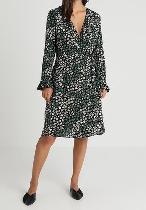 Wrap dress in dark green fabric with white and black star patterns. Long sleeves with ruffle cuffs, V-neckline, and a tie belt at the waist.