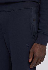 Granatowe spodnie dresowe wykonane z mi�ękkiego materiału, z dwoma bocznymi kieszeniami z guzikami oraz małym haftowanym logo blisko kieszeni.