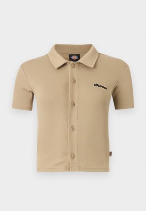 Polo beige à manches courtes avec boutons, col, texture côtelée et petit logo noir « Dickies » sur le côté gauche de la poitrine.