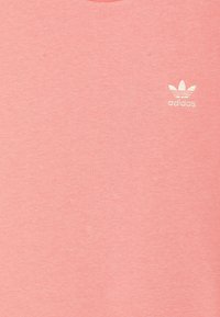 Rosa bomullströja med rund halsringning och korta ärmar. Har en vit Adidas-logotyp på vänster bröst. Slät textur, avslappnad design.