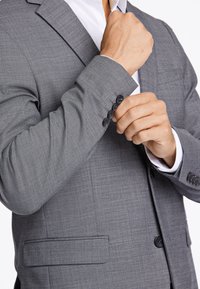 Szary blezer o teksturowanym wykończeniu, z klapami w kształcie litery "notch", jednoprztykowym zapięciem i czterema czarnymi guzikami przy mankietach.