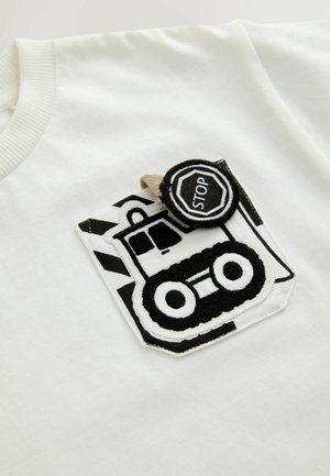 Weißes T-Shirt mit einem schwarz-weißen bestickten Taschenmotiv, das ein Baumaschinenfahrzeug und ein Stoffetikett "STOP" zeigt.