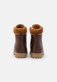 Bruna läderankelboots med en brun konstpälskrage, gummisula och diskret logotyp på hälen. Klassisk rund tå-design.