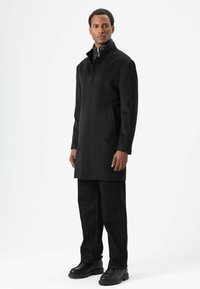 Zwarte jas van een wolmix met een hoge kraag, voorzien van een ritssluiting aan de voorkant en zijzakken, gecombineerd met donkere spijkerbroek en zwarte laarzen.