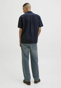 Camisa de manga corta azul marino con un corte holgado, cuello tipo botones y una textura suave, combinada con unos vaqueros de denim liviano de corte suelto en color azul claro.