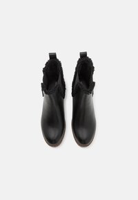 Bottines en cuir noir avec une doublure en feutre noir, des languettes à l'arrière et un bout lisse et arrondi. Semelle plate marron avec texture antidérapante.