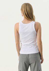 Valkoinen hihaton toppi ribbimateriaalista, jossa on pyöreä kaula-aukko ja slim fit -tyyli. Takapuolella on sileä pinta ilman näkyviä kiinnityksiä tai yksityiskohtia.