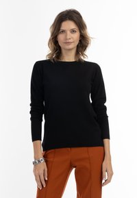 Zwarte trui met lange mouwen en een ronde hals, gecombineerd met oranje broek. Zachte textuur, aansluitend ontwerp, minimale details.