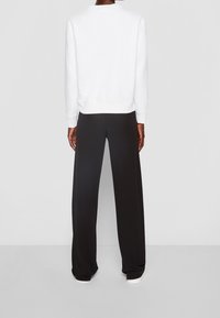 Sudadera blanca con puños y dobladillo acanalados, combinada con pantalones negros de pierna ancha. Textura suave y diseño sencillo sin patrones visibles.